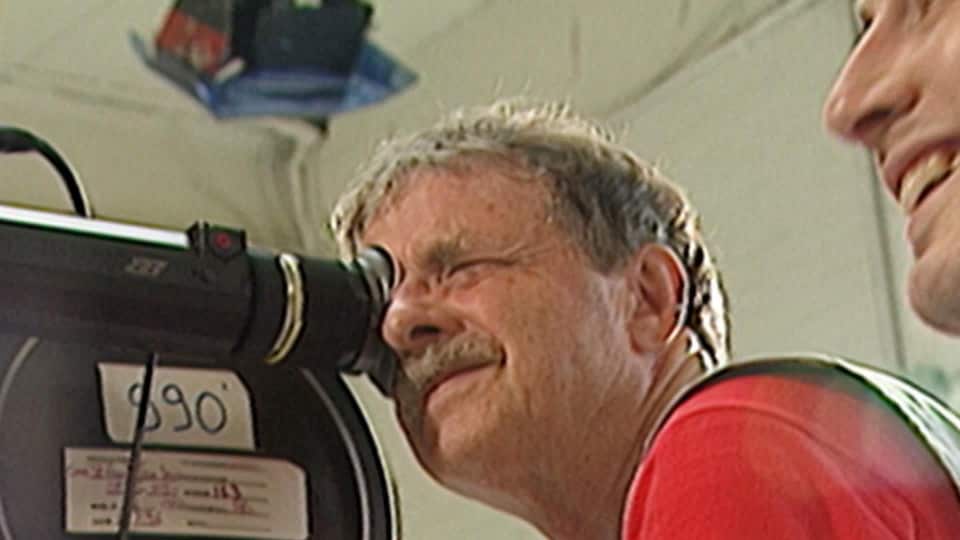 Un homme regardant à travers le viseur d'une caméra cinématographique.