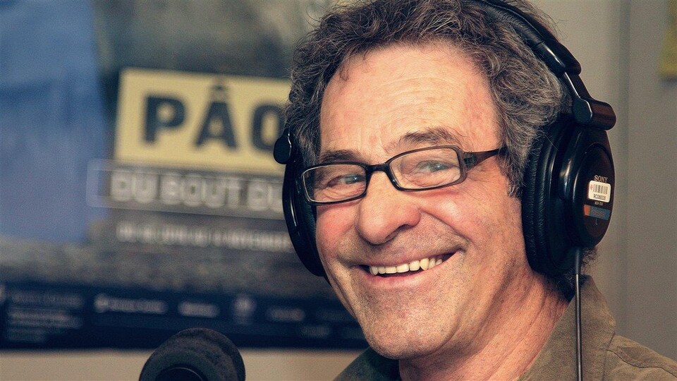 Claude Gauthier portant des écouteurs et devant un micro dans un studio de Radio-Canada.