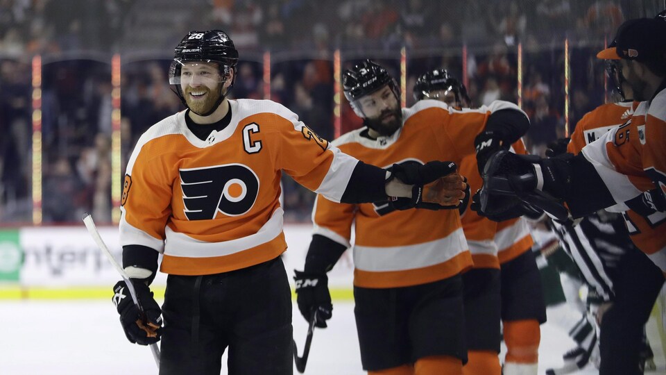 Claude Giroux des Flyers de Philadelphie souriant avec ses coéquipiers après avoir marqué un but lors de la première période d'un match de hockey.