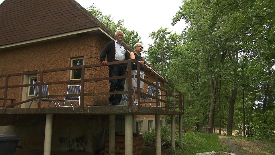 Un couple sur un balcon arrière d'une petite maison brune.