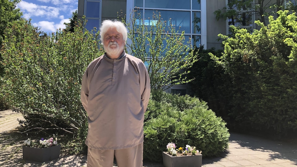 Claude Mercure devant l'usine de Biolyse Pharma à St. Catharines en Ontario. Un homme aux cheveux blanc barbu devant un édifice. 