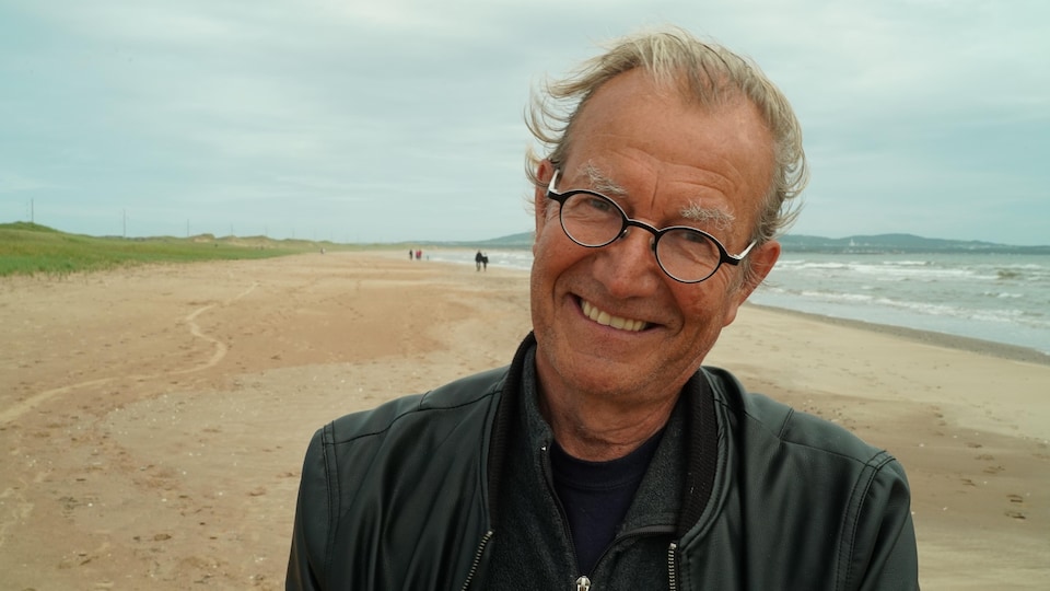 Claude Roy sourit sur une plage.