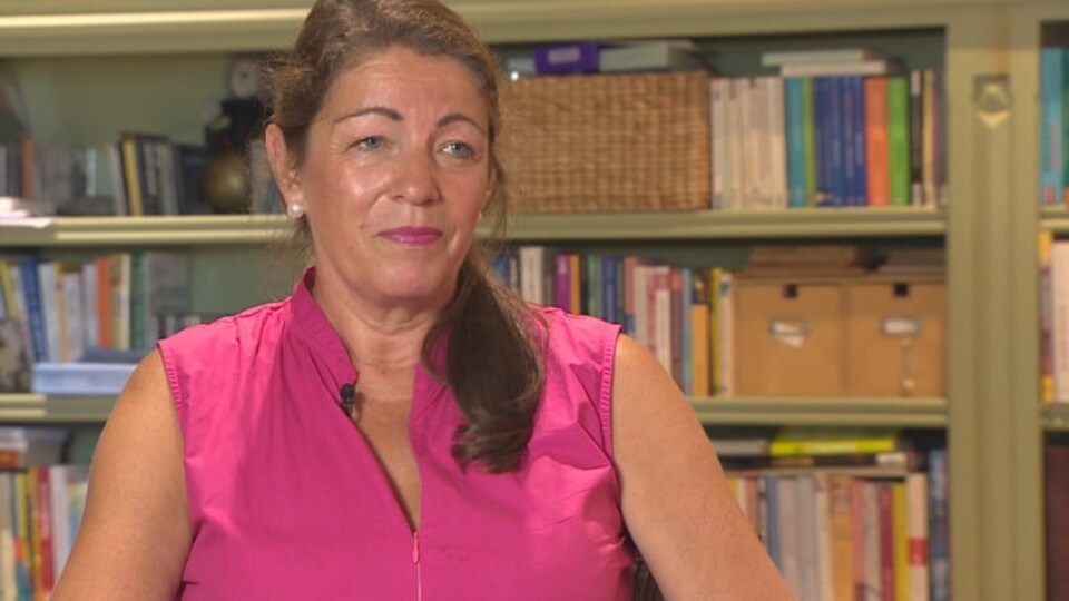 La dame est assise devant des étagères remplies de livres.