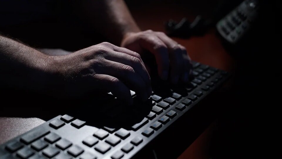 Des mains sur un clavier d'ordinateur dans la pénombre.