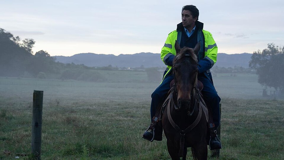 L'acteur, montant à cheval et portant une veste jaune de policier.