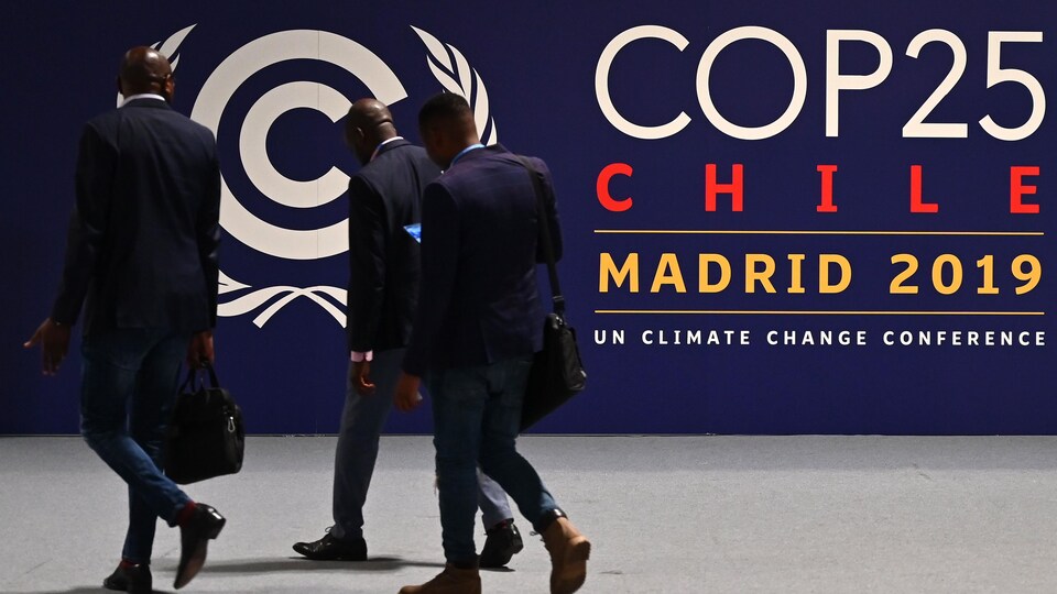 Des hommes entrent devant un panneau qui indique le site de la COP25 à Madrid.
