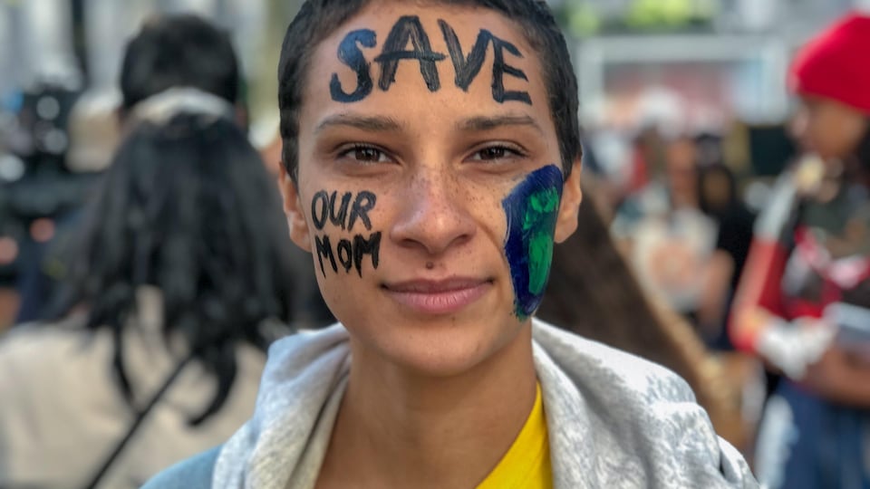 Un manifestant dont le visage a été peint et sur lequel il est écrit «sauvez notre mère».