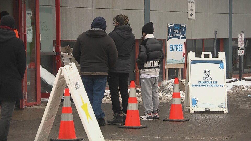 Trois personnes attendent devant un centre de dépistage.