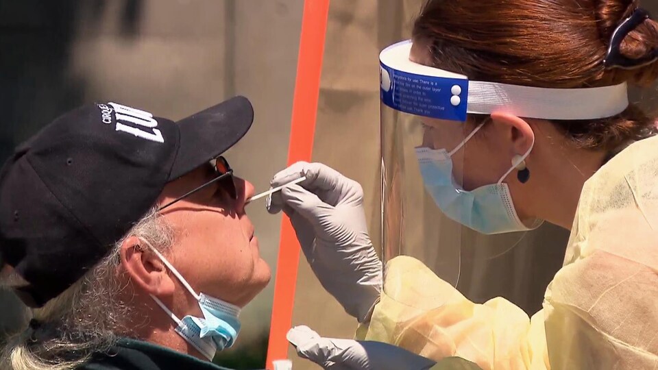 Une infirmière qui porte masque, visière et gants prend un prélèvement dans le nez d'un homme.