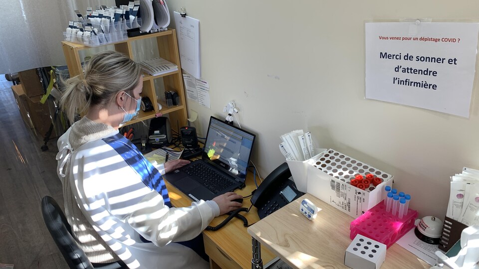 Une infirmière est assise devant son ordinateur avec des tests de dépistage de la COVID à sa droite.