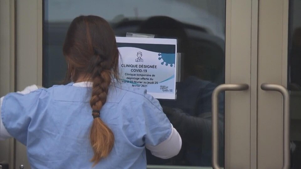 Une femme qui colle une affiche indiquant qu'il s'agit d'une clinique désignée COVID-19.
