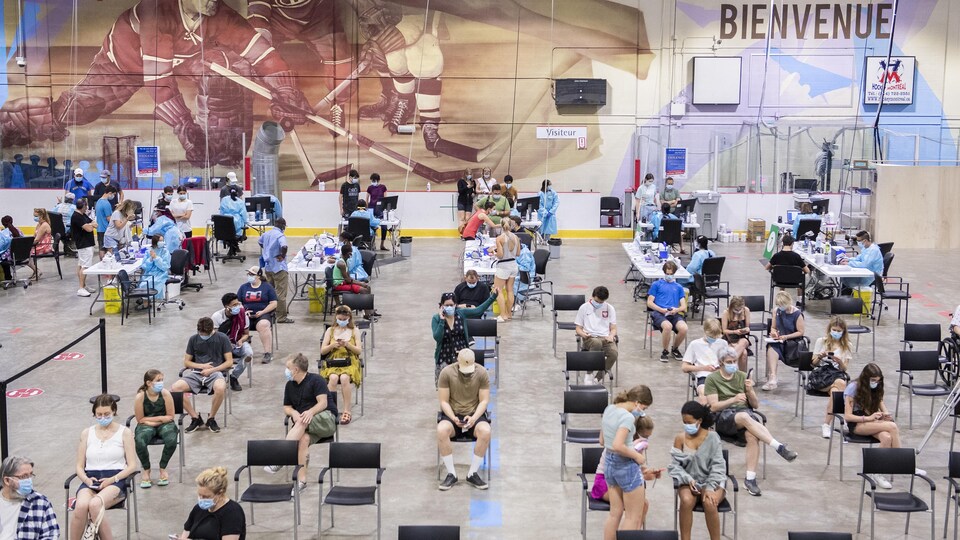 Des gens attendent dans une grande salle d'une clinique de vaccination, à Montréal.