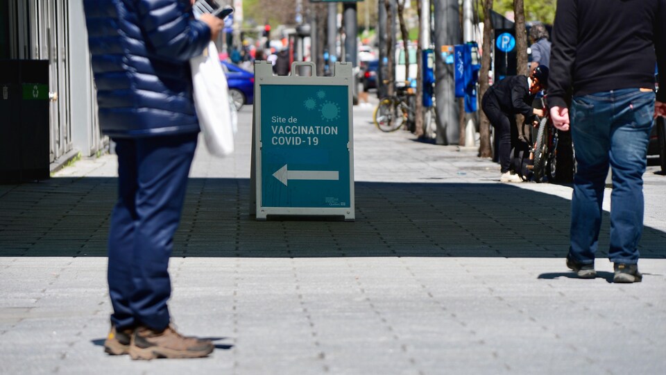 Un panneau posé au milieu du trottoir indique l'entrée d'une clinique de vaccination.