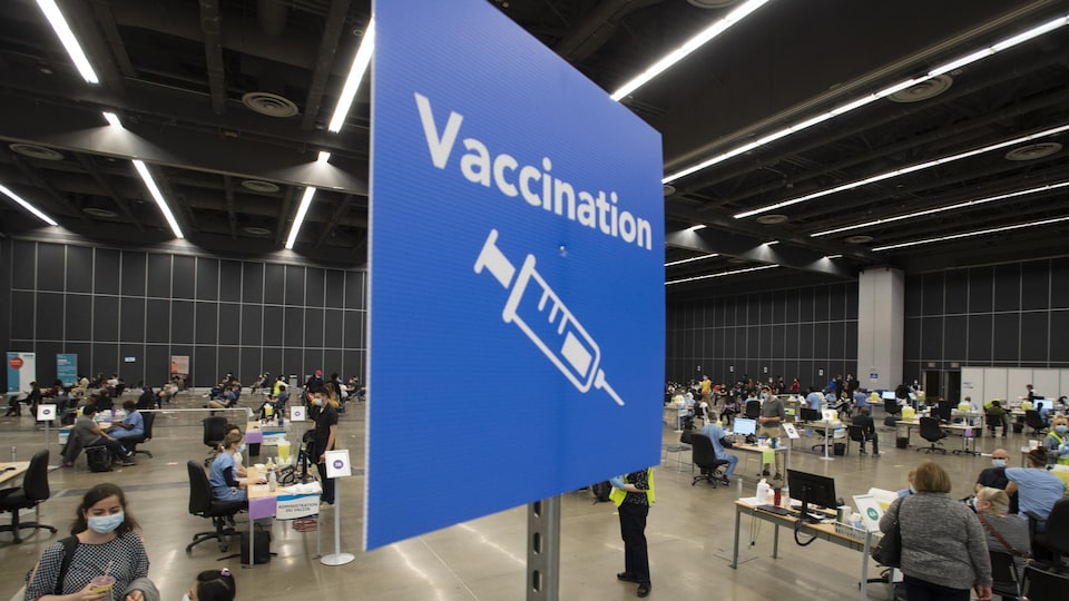 Des dizaines de personnes se promènent dans une grande salle, où se trouvent de petites stations de vaccination.