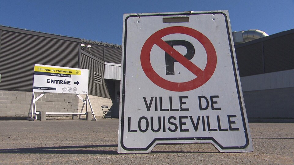 Une affiche de la Ville de Louiseville qui interdit le stationnement à cet endroit, devant une pancarte indiquant qu'il y a une clinique de vaccination.