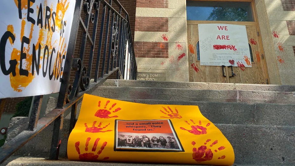 Les marches devant la co-cathédrale Saint-Paul. Des mains sont tracées sur la porte de l'église. Sur la porte d'entrée, la pancarte mentionnant ''nous sommes désolés'' en anglais, a été vandalisée.