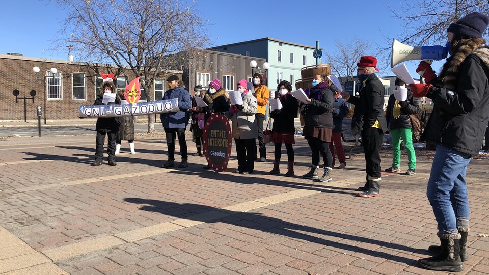 Une quinzaine de personnes chantent avec des pancartes qui dénoncent le projet de Gazoduq et GNL Québec.
