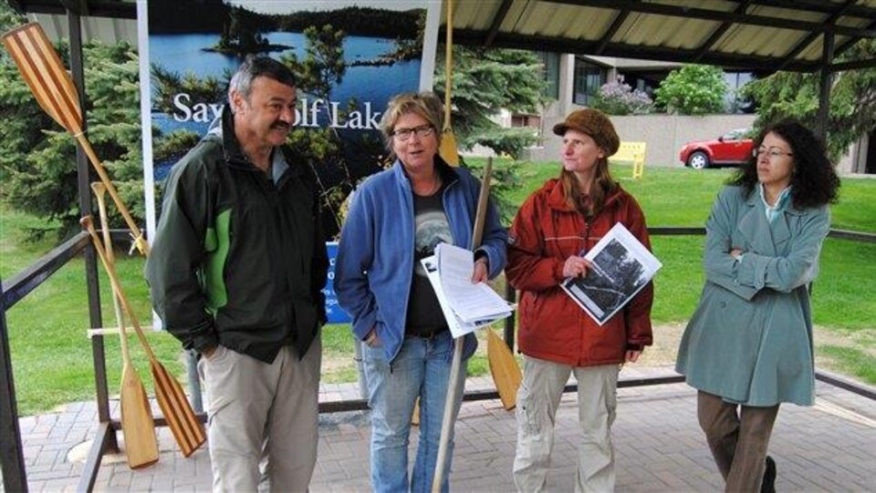 Quatre personnes se tiennent debout devant une pancarte sur laquelle est écrit « Save Wolf Lake ».