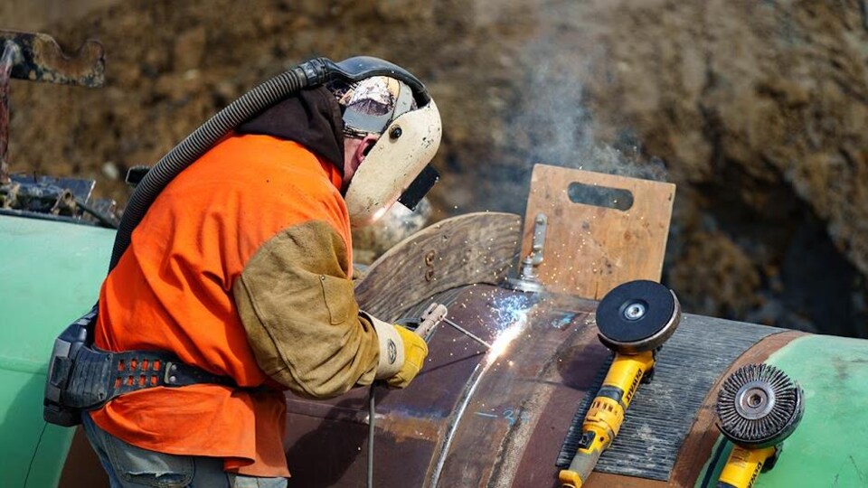 Un soudeur travaille sur un joint entre deux sections de pipeline.