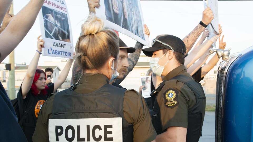 Des activistes tenant des pancartes s'interposent devant des agents de la SQ masqués.