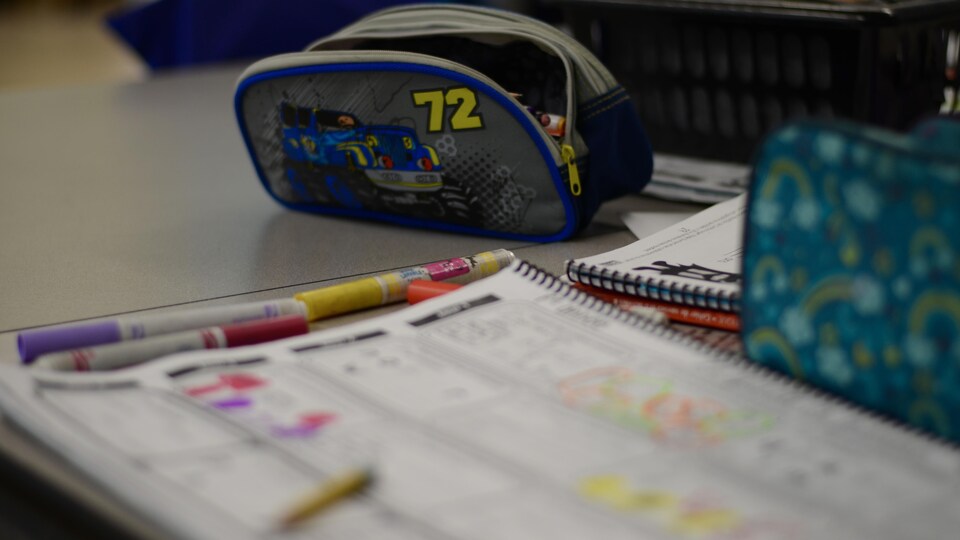 Coffre à crayons, crayons et cahier d'exercices sur un bureau.
