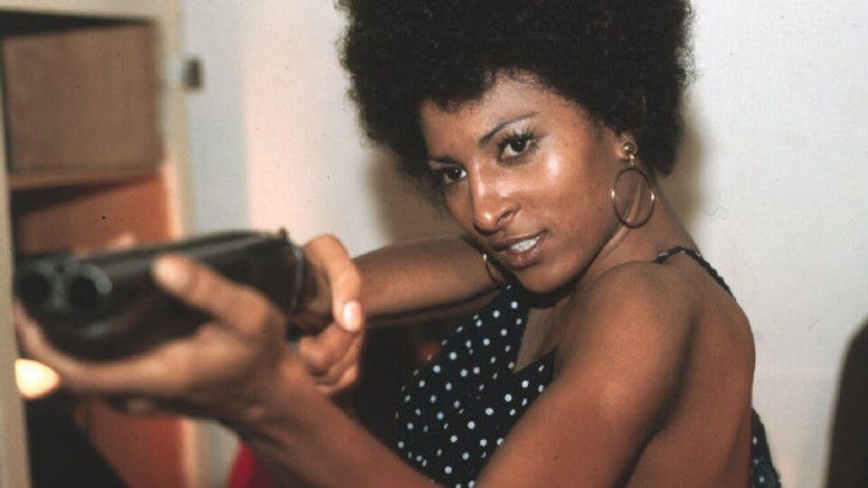 Une femme tenant un fusil à canon scié vise quelqu'un hors cadre dans une scène du film coffy.