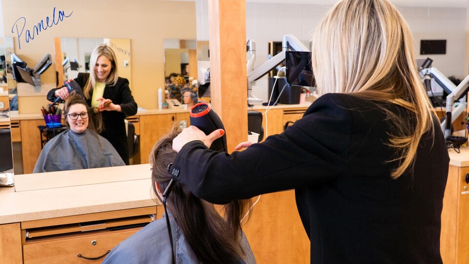 Une coiffeuse coiffe les cheveux d'une cliente en souriant.