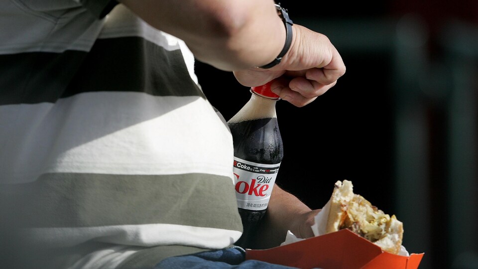 Un homme obèse ouvre une bouteille de coke.