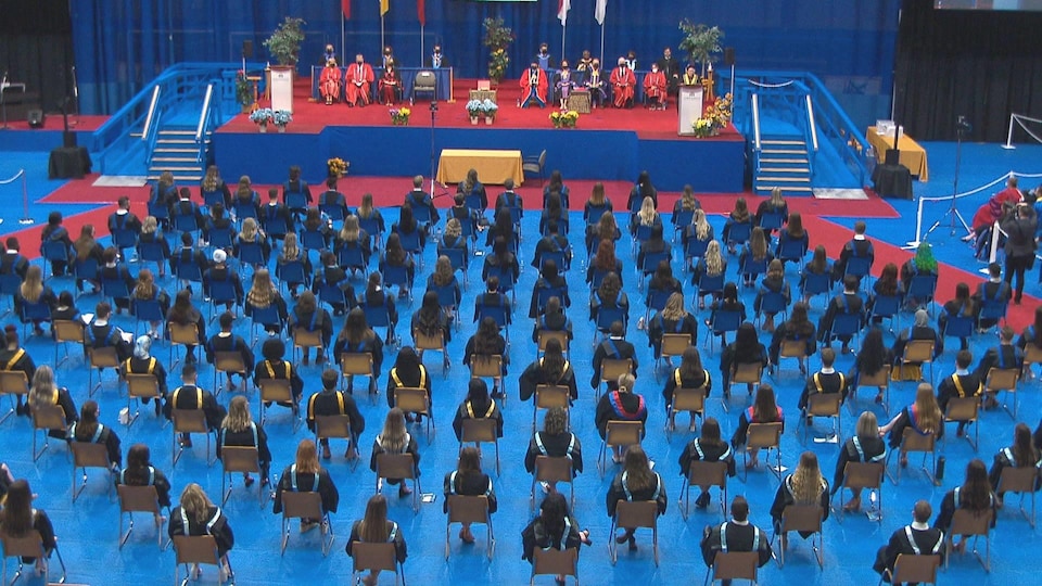L'ensemble de la salle prise en photo. Les diplômés sont vêtus de leur toge et assis sur des chaises.