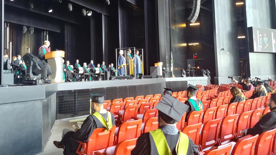 Des étudiants avec toge et mortier regardent la remise de diplômes sur la scène.