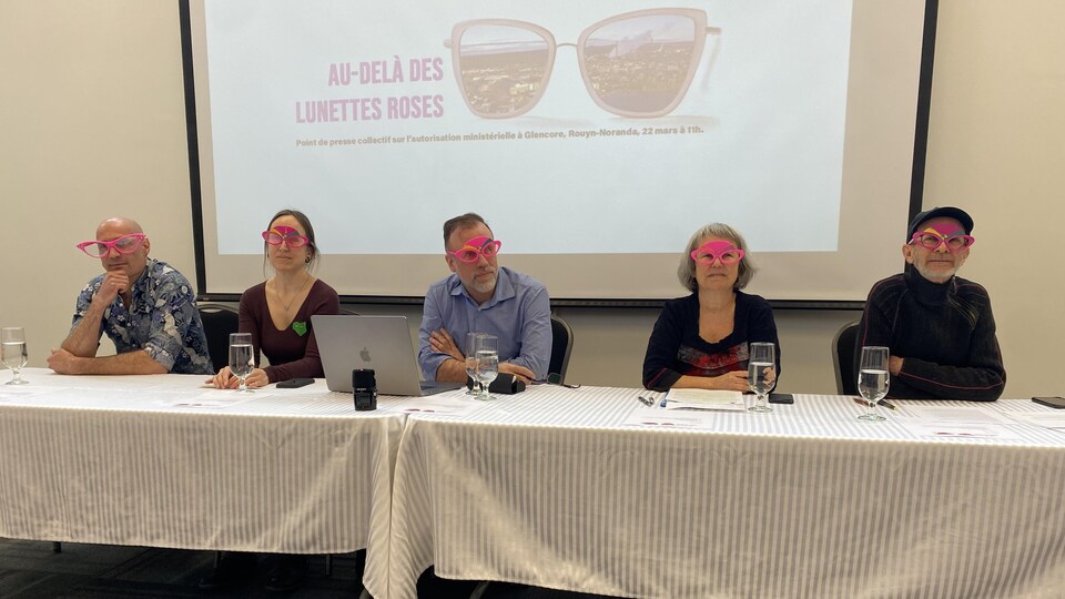 Cinq personnes assises derrière une table et portant des lunettes roses, en conférence de presse.