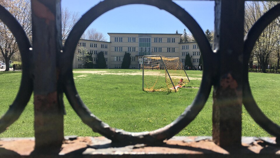 Le terrain de soccer d'une école vu à travers une clôture en fer forgé.