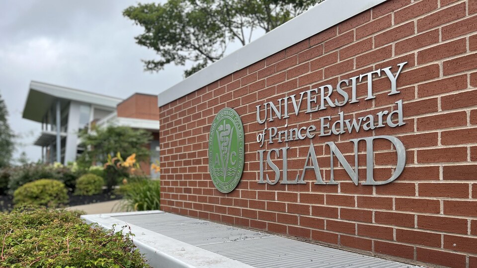 Un muret en briques rouges sur lequel sont accrochés le logo rond et vert du collège vétérinaire et les lettres formant les mots University of Prince Edward Island.