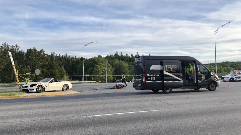 Une décapotable abimée à l'avant, une moto au sol et un camion de police.