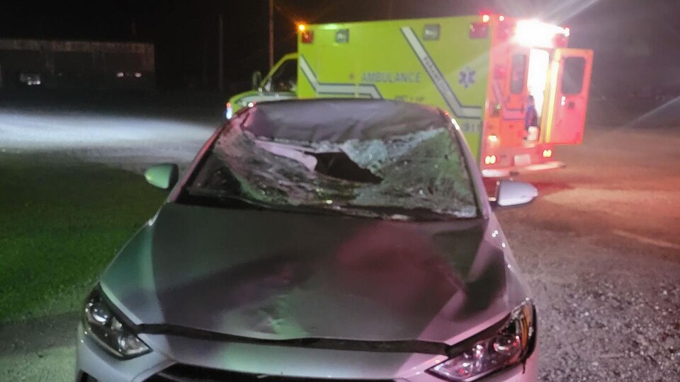 Une voiture accidentée et une ambulance en arrière-plan.