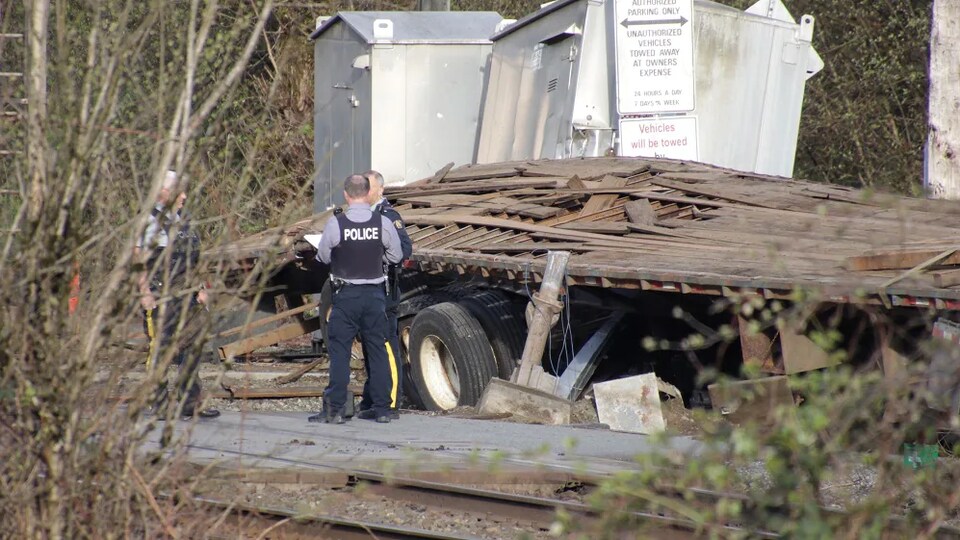Deux policiers en uniforme sont sur une voie ferrée à côté des débris du plateau d'un camion-remorque à la suite d'une collision entre la remorque et un train, le jeudi 21 avril 2022.