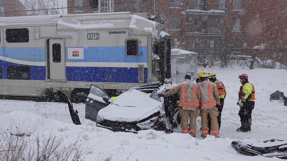 Une voiture emboutie par un train entourée de pompiers et secouristes.
