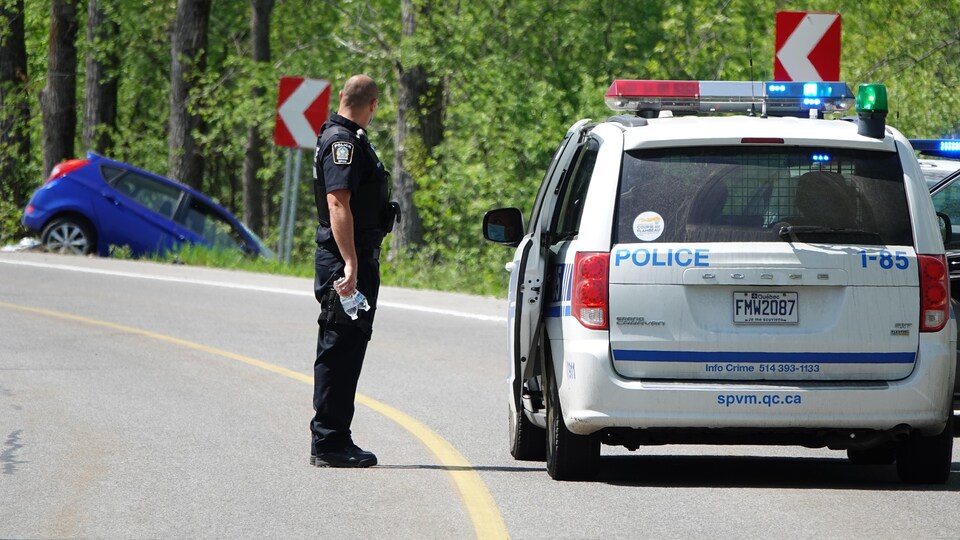 Un policier observe une voiture bleue en bordure de la route.
