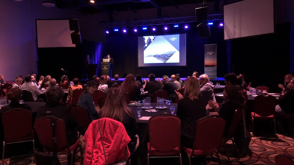Des dizaines de personnes assistent au colloque de l'industrie touristique, dans une grande salle de l'Hostellerie Baie-Bleue, à Carleton-sur-Mer.
