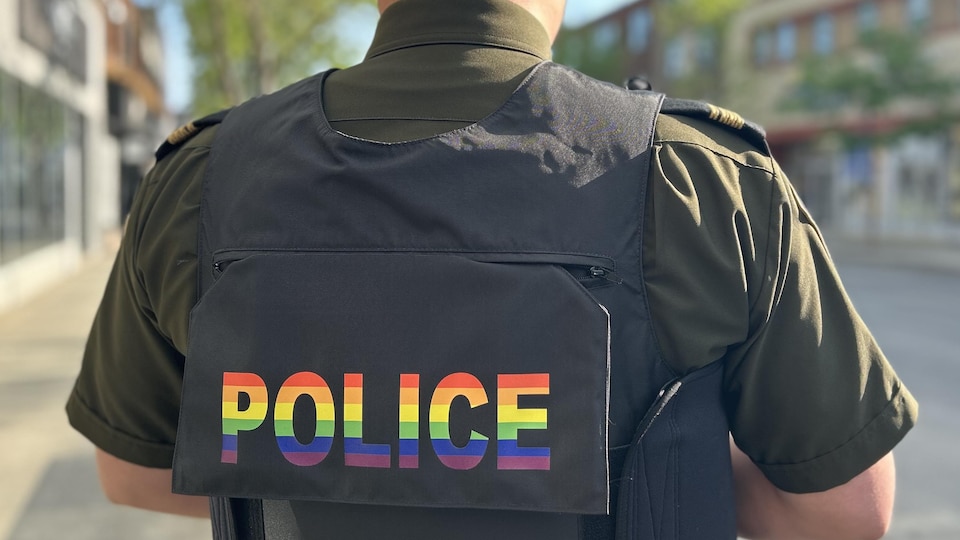 La police de caractère du mot Police sur la veste d'un policier a été modifiée aux couleurs de la communauté LGBTQ+.