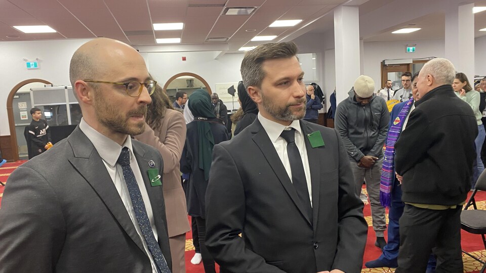 Deux hommes discutent devant la caméra. 