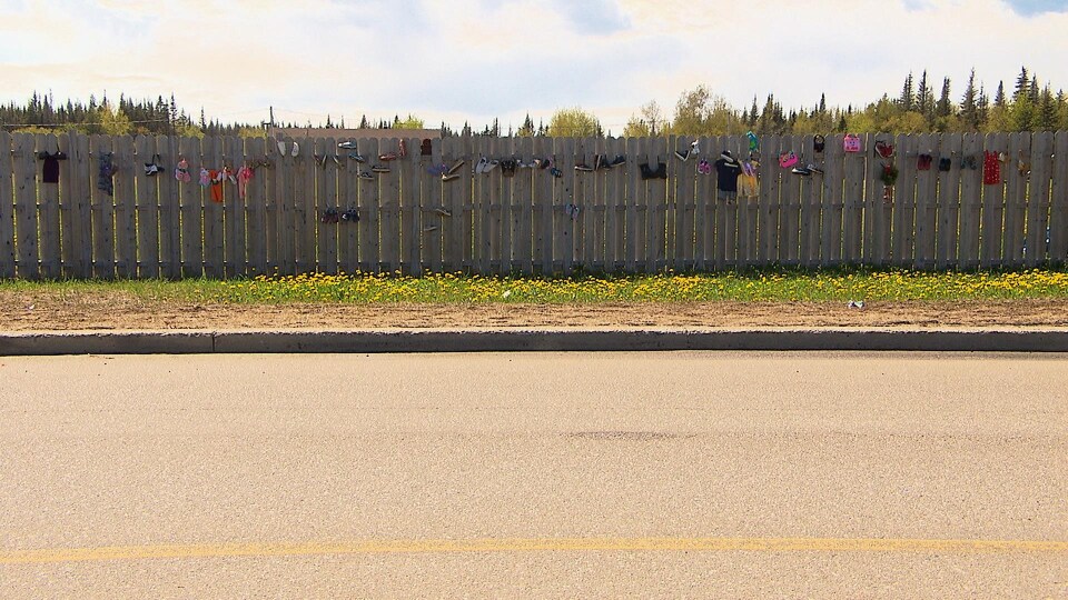 La clôture qui borde le site Innu Nikamu est remplie de souliers et de vêtements d'enfants.