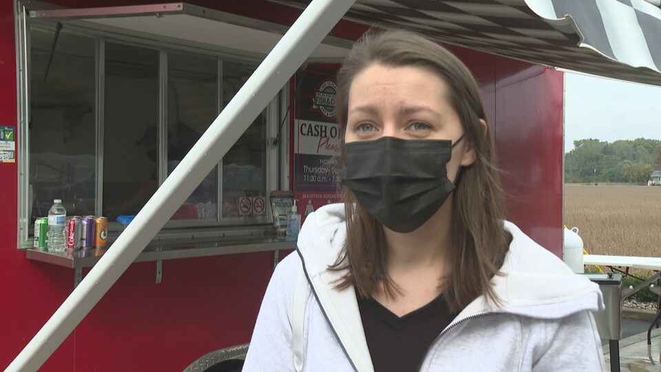 Une femme porte un masque devant un camion de nourriture.