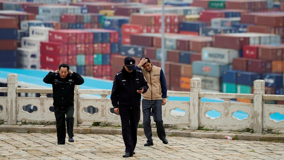 Des gardiens de sécurité marchent dans un port. En arrière-plan, des centaines de conteneurs. 