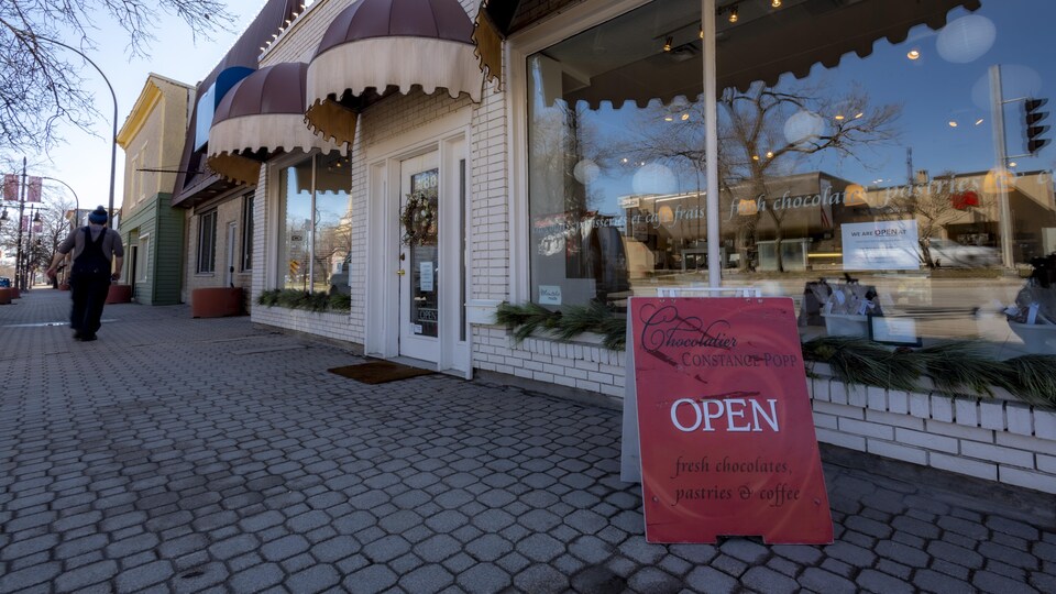 La devanture de la boutique devant laquelle une affiche posée sur le trottoir indique que le commerce est ouvert.