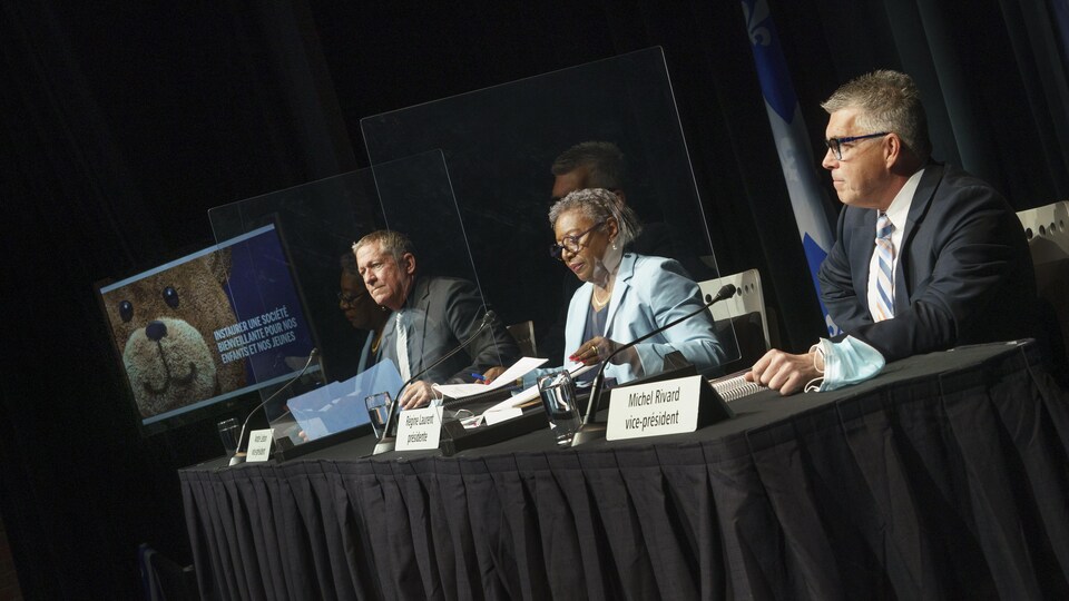 Trois personnes sont assises à une table et font une présentation.