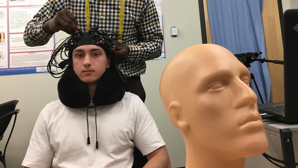 Un jeune homme a un bonnet composé d'électrodes sur sa tête. 