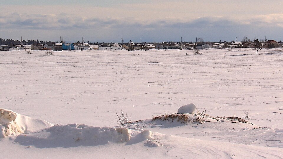 Au bout d'un champ enneigé, des maisons sont alignées.