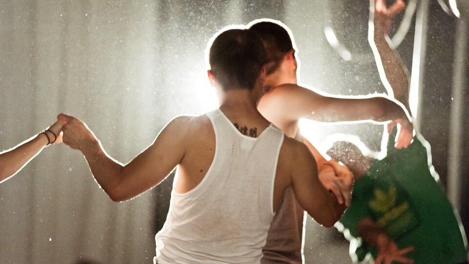 Des hommes dansent de dos avec une lumière en arrière.