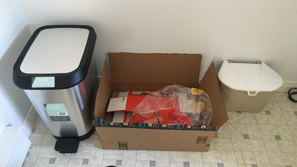 Une poubelle, un bac de carton et un petit bac de compost un à côté de l'autre sur le plancher. 